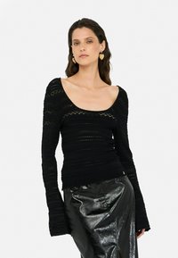 Black long-sleeve top featuring textured knit patterns, a scoop neckline, and flared sleeves, paired with a shiny black skirt.