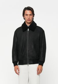 Black faux leather jacket with a large black shearling collar, ribbed cuffs, and a front zipper. Simple design, matte texture.