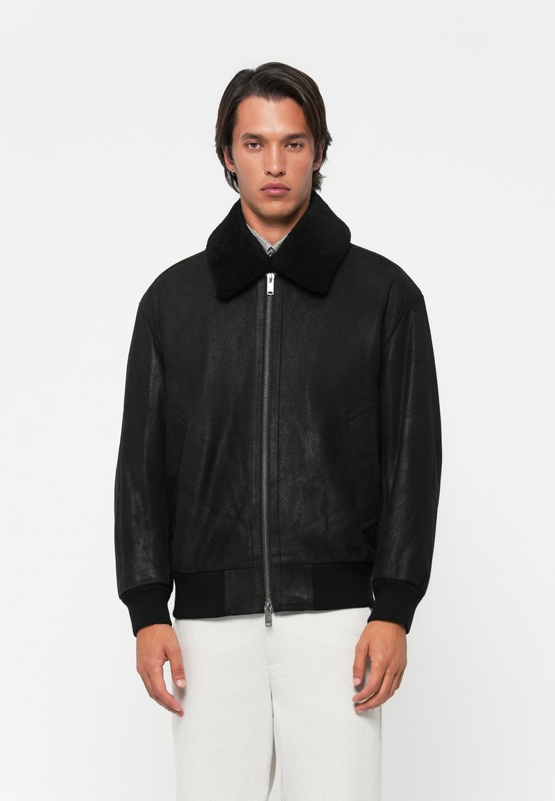 Black faux leather jacket with a large black shearling collar, ribbed cuffs, and a front zipper. Simple design, matte texture.