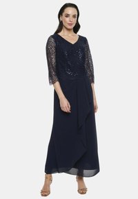 Granatowa sukienka wieczorowa z koronkowym gorsetem ozdobionym cekinami, rękawami o długości trzech czwartych oraz drapowaną spódnicą o asymetrycznym fasonie.