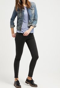 Jeansjacka, ljusblus med prickar, svarta tajta jeans och svarta snörskor. Funktioner inkluderar knappar och uppvikta ärmar.