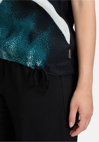 Svarta träningsbyxor med en överdel i turkos och vit mönster, med en dragsko i midjan och en slät tygtextur.