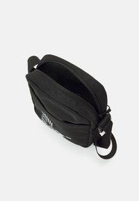 Borsa a tracolla nera in tessuto con chiusura a zip, dotata di una tasca anteriore e tracolla regolabile. L'interno è foderato con un materiale liscio.