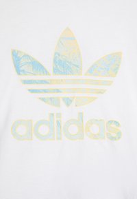 T-shirt branca de algodão com um logótipo trefoil da Adidas em azul e amarelo e o nome da marca "adidas" em cores a condizer logo abaixo.
