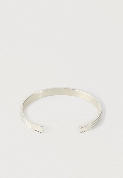 Otwarte srebrne bransoletki z paskami grawerowanymi w pobliżu końców oraz małymi oznaczeniami tekstowymi, w tym "le gramme" i "30g".