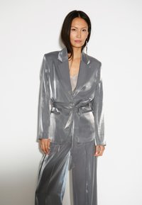 Zilveren metallic blazer met bijpassende broek, voorzien van een strikceintuur, lange mouwen en een gladde, glanzende textuur.