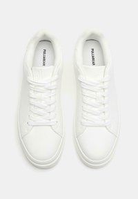 Sneakers sintetiche bianche con una finitura liscia, dotate di lacci, colletto imbottito e un marchio discreto sulla soletta. Design e forma classici.