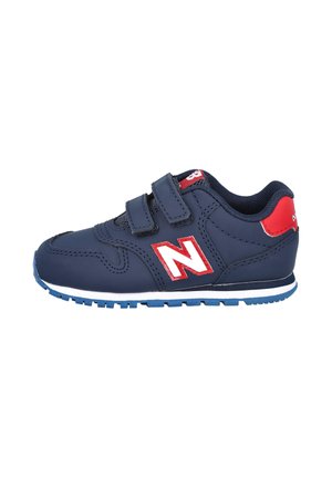Zapatillas infantiles azul marino con detalles rojos, dos tiras de velcro, suela de goma y detalles blancos. Presenta el logo de New Balance en el lateral.