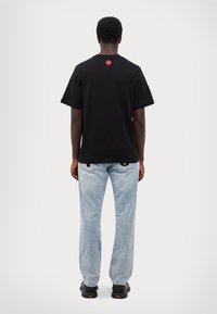 Black cotton t-shirt with short sleeves, featuring a red circular logo at the back. Paired with light blue jeans and black shoes.