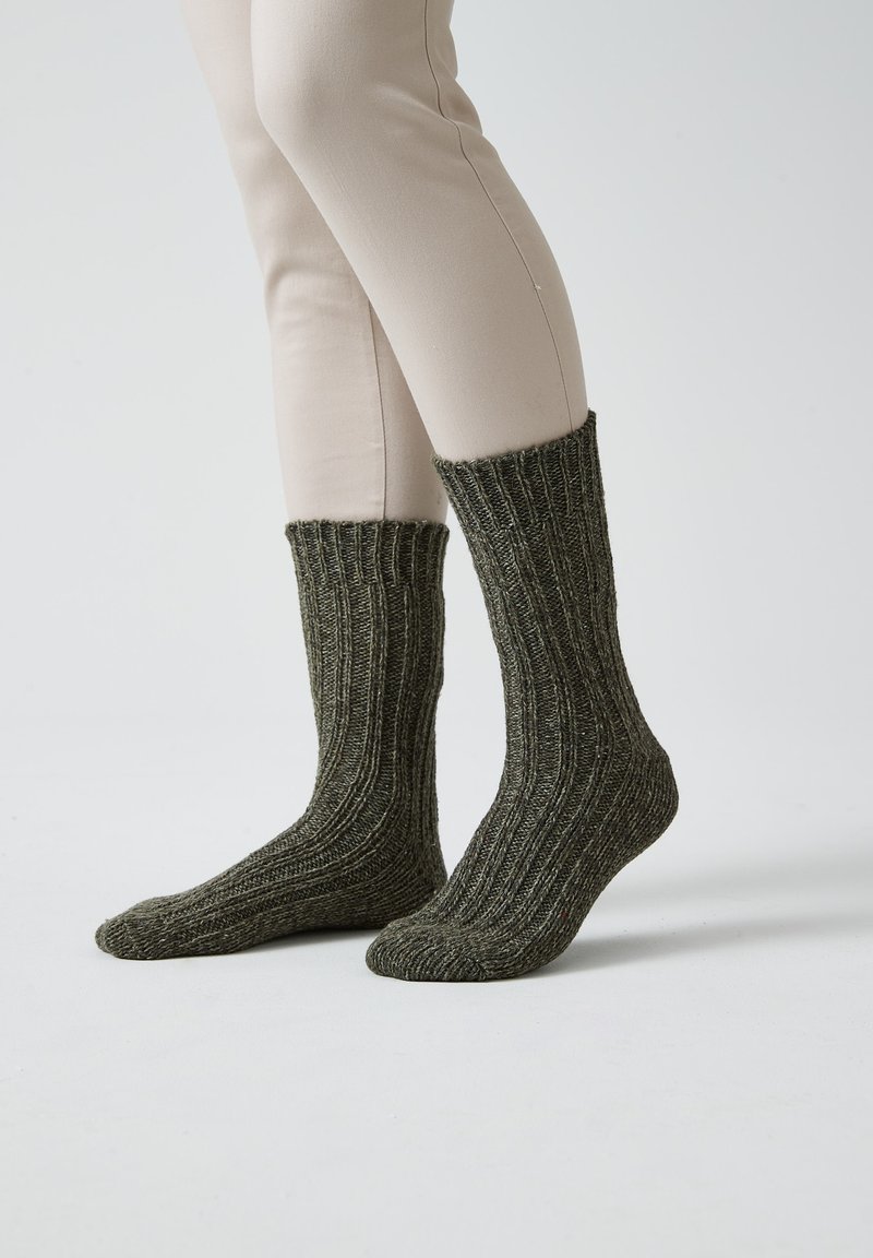 Calze verdi a coste realizzate in tessuto di maglia testurizzata, con un risvolto alto e una vestibilità aderente alla caviglia. Indossate con pantaloni chiari.