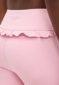 Κοντινό πλάνο ενός ατόμου που φοράει αθλητικό κολάν ανοιχτού ροζ χρώματος με ελαστική μέση και το λογότυπο "Ted Baker Sport".