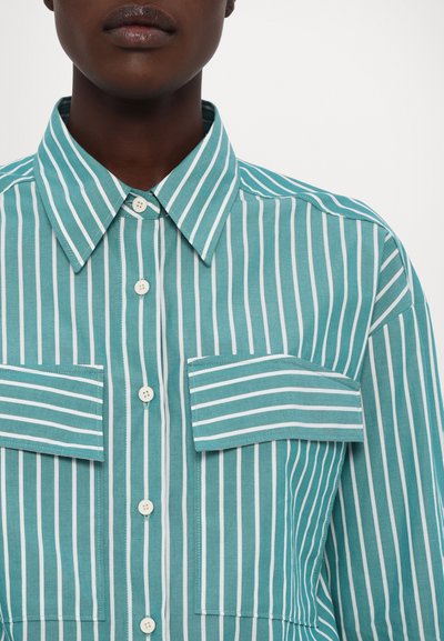 Cămașă striped în nuanțe de teal și alb, cu închidere butonată, guler și două buzunare pe piept. Fabricată din bumbac cu o textură netedă.