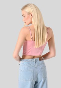 Top corto rosa con spalline sottili, abbinato a jeans a vita alta blu chiaro con tasca posteriore e cintura testurizzata.