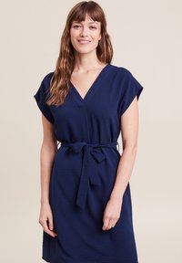 Marineblaues Kleid mit kurzen Ärmeln, V-Ausschnitt und einem Stoffgürtel in der Taille. Strukturierter Stoff mit lockerer Passform.