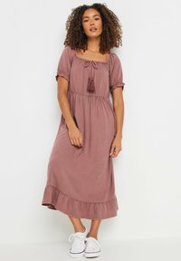 Vestido midi malva con mangas cortas abullonadas, escote cuadrado, detalles de cordón y dobladillo con volantes, combinado con zapatillas blancas.