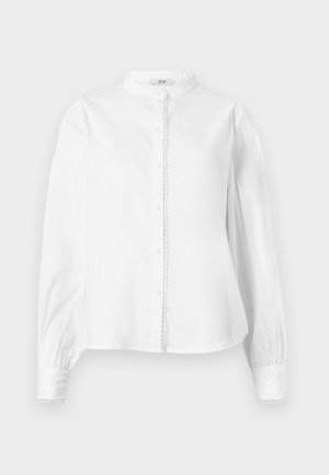 Balta garām piedurknēm blūze ar augstu apkakli, priekšējo pogu aizdari, nedaudz pūkainām piedurknēm un viļņotu apdari ap pogām un aprocēm.