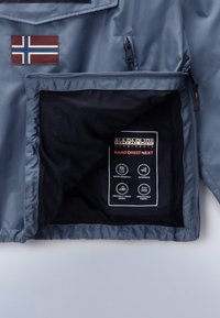 Gray jacket interior with mesh lining displays fabric care tags, including symbols for water-resistant, windproof, and breathable features.