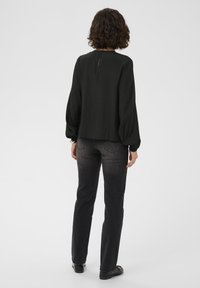 Zwarte blouse met lange mouwen, ronde halslijn en een splitdetail op de rug, gecombineerd met donkergrijze rechte jeans. Gladde stof, losse fit.