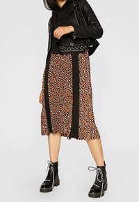 Gonna leopardato marrone con strisce laterali nere, abbinato a una giacca di pelle nera e stivali neri chunky, mentre porta una piccola borsa nera.