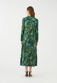 Abito lungo a maniche lunghe di colore verde con stampa floreale, caratterizzato da una combinazione di tonalità di blu scuro e chiaro, realizzato in un materiale morbido con una silhouette fluente.