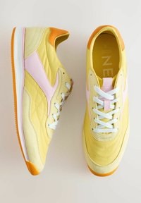 Sneakers gialli con accenti rosa, lacci bianchi e tacchi arancioni. Materiali lisci e testurizzati, con punta arrotondata e suola in gomma.