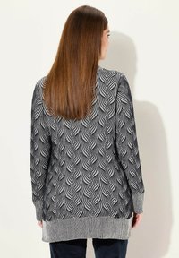 Cardigan a maniche lunghe con motivo a onde in bianco e nero, texture lavorata a maglia, presenta polsini e orlo a coste, taglio di lunghezza media con spacchi laterali.