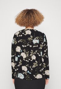 Czarna bluzka w kwiaty z długimi rękawami, zdobiona dużymi kremowymi i niebieskimi kwiatami, zielonymi liśćmi oraz falbaną z tyłu.