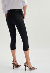 Jeans negros cortos con un diseño ajustado, que presentan una ligera abertura en el dobladillo, combinados con zapatos de tacón alto de estampado de leopardo.