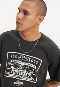 T-shirt en coton noir avec un grand imprimé graphique blanc comportant du texte et des images. Manches courtes, col rond et texture douce.