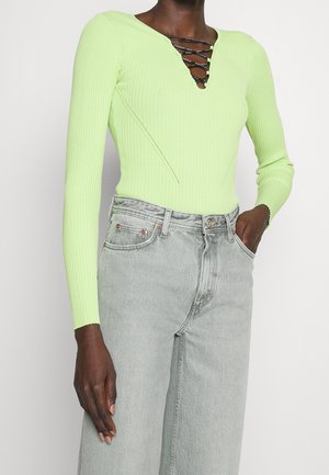 Body a maniche lunghe verde lime a costine con scollo a V e dettagli con lacci, abbinato a jeans grigi chiari a gamba larga.