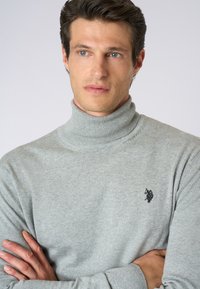 Maglione grigio a collo alto realizzato in morbido tessuto a maglia, con un design aderente e un piccolo logo nero sul petto.