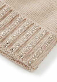 Beżowy dziergany dodatek z rytmicznym prążkowaniem, ozdobiony rozmieszczonymi przezroczystymi kryształkami, które dodają faktury i atrakcyjności wzorowi.