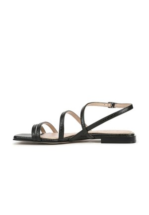 Black strappy sandal with a flat sole, featuring textured material and crisscross design. Adjustable ankle strap and minimalistic style.