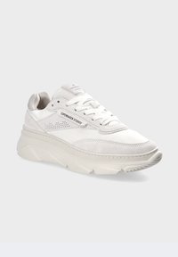 Bílé tenisky s kombinací hladké a strukturované kůže. Masivní podešev, šněrovací design a boční perforace pro ventilaci.