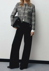 Veste en tweed noir et blanc au design court et boutons ronds, assortie à un pantalon noir à jambes larges et un sac à main noir.