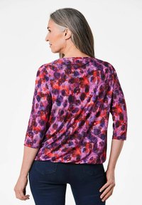 Mehrfarbige Bluse mit einem floralen Muster in Lila-, Rot- und Rosatönen. Das Design hat Dreiviertelärmel und einen runden Ausschnitt.