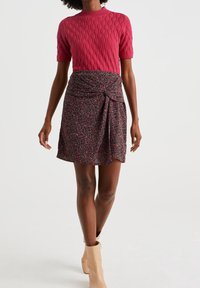 Růžový pletený top s texturou a krátkým rukávem v kombinaci s květinovou zavinovací sukní se svázaným detailem. Outfit doplňují béžové kotníkové boty.