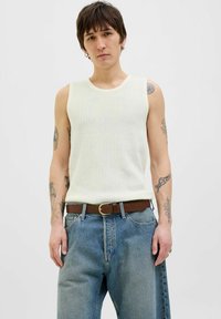 Witte geribbelde mouwloze top met ronde hals, gecombineerd met lichtblauwe losse jeans en een bruine riem, met een gestructureerd oppervlak en zichtbare tatoeages.