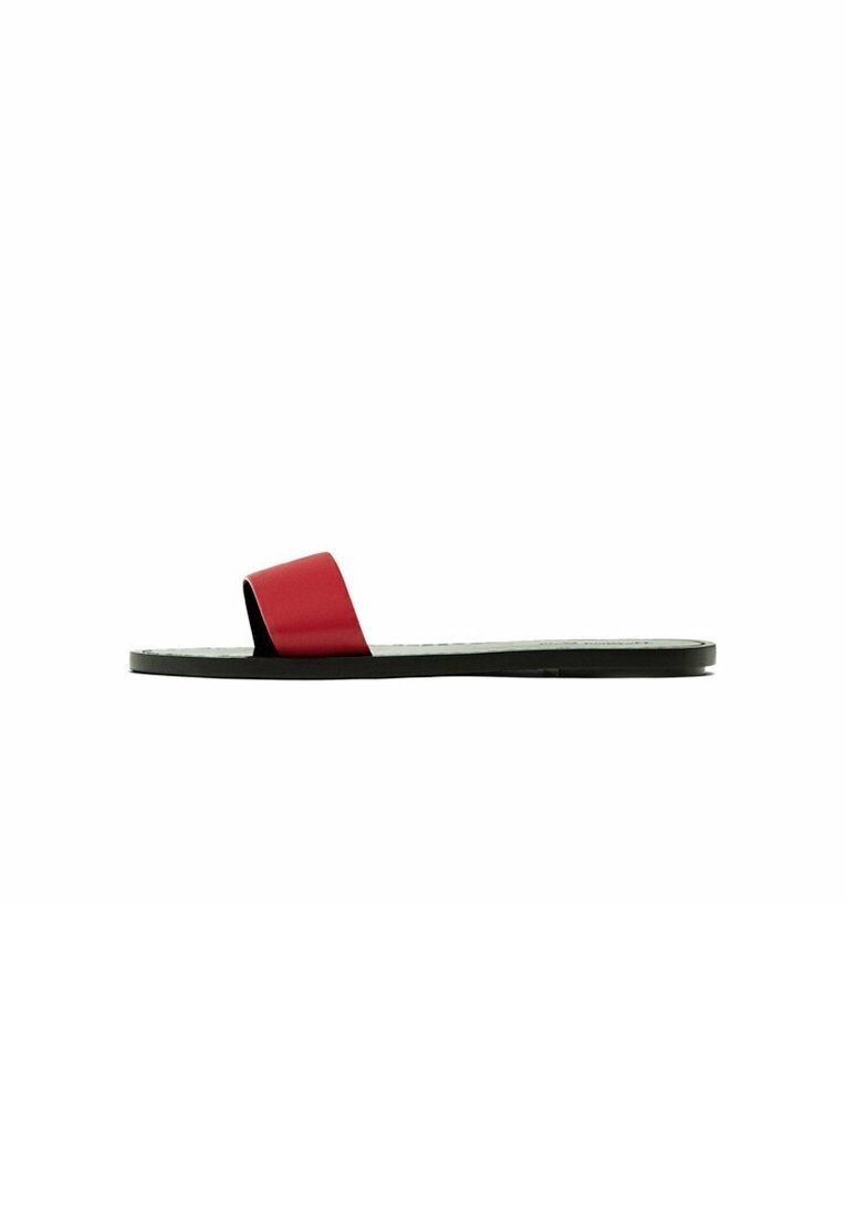 Sandale plate noire à enfiler avec une large bride rouge unique sur le dessus du pied, vue de profil sur fond blanc.
