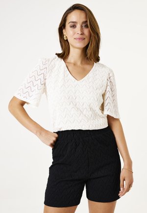 Blouse blanche texturée avec un décolleté en V et des manches courtes, accompagnée de shorts noirs texturés. Les deux vêtements présentent un motif.