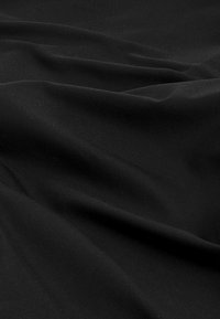 Tissu noir avec des plis doux et une texture de tissage diagonal visible créant des ombres et des reflets subtils.