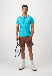 A turquoise polo shirt with a white collar, paired with brown shorts. The person is holding a tennis racket and wearing white athletic shoes.