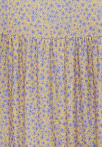 Kukallinen mekko, jossa on pieniä violetteja kukkia keltaisella taustalla, rypistyneellä pinnalla ja frilla muotoilulla vyötäröllä.