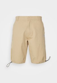 Shorts beiges à coupe décontractée, dotés d'un cordon de serrage ajustable à l'ourlet et d'une petite étiquette logo sur le côté gauche. Matière en coton.