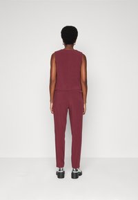 Vinfärgad ärmlös topp och matchande tapered byxor, tillverkade av ett smidigt tyg. Har en subtil bakseam och en elegant  ankle-length passform.