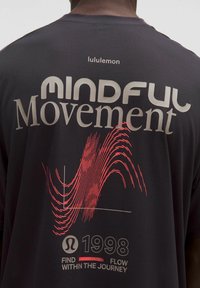Tricou sportiv negru din material respirabil. Are inscripția "MINDFUL Movement" în gri deschis, un grafic cu val roșu și logo-ul "lululemon" pe spate.