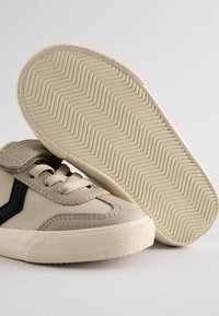Beżowe zamszowe sneakersy z czarnymi akcentami, z teksturowaną gumową podeszwą i beżowymi sznurówkami. Wzór w jodełkę na podeszwie.