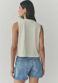 Ljusbeige ärmlös topp med ett texturerat mönster, kombinerad med högmidjade blå denimshorts. Minimalistisk design med en kortad passform.