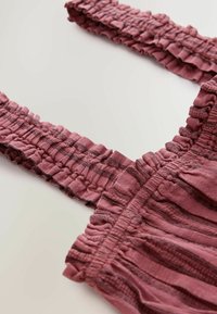 Detailed close-up of dusty rose fabric with elastic smocked straps and subtle horizontal stripe texture on a light background.