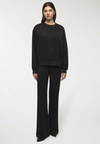 Felpa nera con testo in rilievo "SELFLOVE Club", abbinata a pantaloni neri a vita alta e a gamba larga. Entrambi realizzati in materiale morbido.